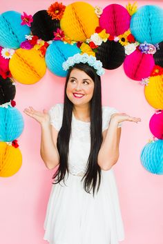 a woman in a white dress is holding her hands out to the side with colorful paper decorations behind her