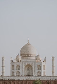 a large white building with many pillars and domes on it's sides in front of a brick wall