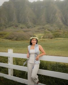 a woman standing next to a white fence in front of a lush green mountain range