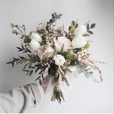 a person holding a bouquet of white flowers in their hand with greenery on the side