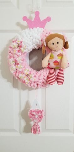 a pink wreath with a girl doll hanging from it's side on a door