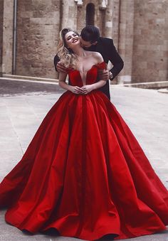 a man in a tuxedo kissing a woman in a red dress on the street