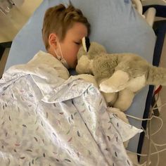 a young boy laying in a hospital bed next to a stuffed animal and wearing an oxygen tube