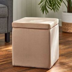 a beige storage box sitting on top of a wooden floor next to a chair and potted plant