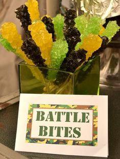 a glass vase filled with yellow and green gummy bears next to a card that says battle bites