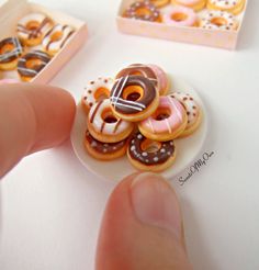 a hand is holding a miniature donut on a small plate next to two boxes of doughnuts