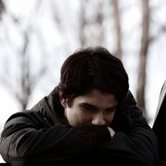 a young man leaning his head on top of a bench in front of trees and snow