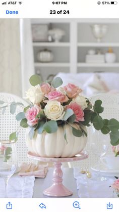 a white pumpkin decorated with flowers and greenery on top of a pink cake plate