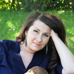 a woman holding a small child in her lap while sitting on the grass with trees in the background