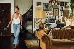 a woman walking through a living room with lots of pictures on the wall and furniture