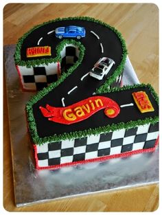 a birthday cake that is shaped like a number two with cars on the road and grass