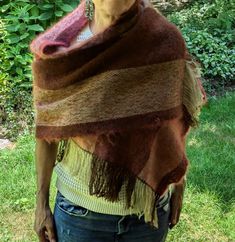 a woman standing in the grass wearing a brown and tan shawl