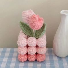 a crocheted vase with two flowers on it next to a small stack of balls