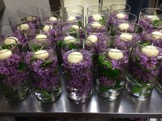 many glasses filled with flowers and candles on top of a metal table next to each other