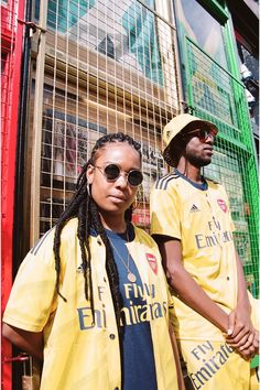 two people standing next to each other in front of a caged area wearing yellow jackets and sunglasses