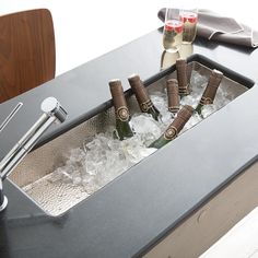 four bottles of champagne are in an ice bucket on a counter top with wine glasses and utensils