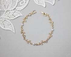 a gold bracelet with white pearls and leaves on the side, next to a lace doily