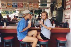 two young women sitting at a bar drinking coffee and talking to each other while another woman looks on