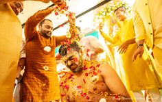 a group of men standing around each other in front of a man with flowers on his face