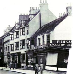 an old black and white photo of people walking down the street in front of shops