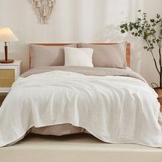 a bed with white linens and pillows in a neutral bedroom, next to a small potted plant