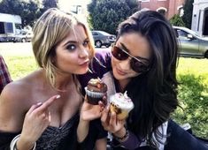 two beautiful young women eating cupcakes in a park together on a sunny day