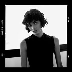 a black and white photo of a woman with curly hair wearing a sleeveless top