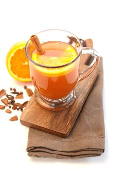 a glass mug filled with orange juice next to an orange slice and cinnamon on a cutting board