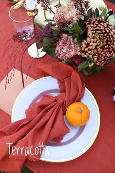 an orange sits on a white plate next to a red table cloth and some flowers