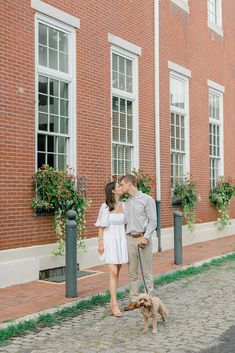 a man and woman are walking their dog down the street in front of a brick building