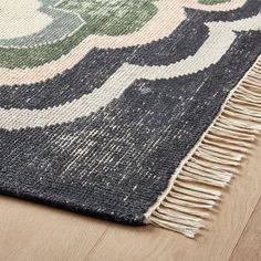 an area rug with fringes on top of the wooden floor and a blue, green, white and black design