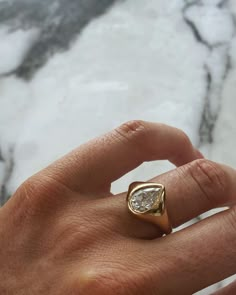 a person's hand holding a gold ring with a pear shaped diamond on it