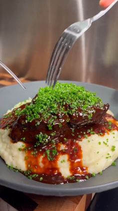 someone is spreading sauce on mashed potatoes with green garnish and sprinkles