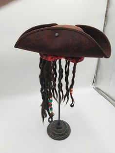 Complete your Pirate Costume this season with this Deluxe Child Caribbean Pirate Hat with Attached Dread Locs Wig. Perfect for Halloween, Cosplay, Theater and more! Featuring a tri-corne hat with attached brown faux braided hair with beads accented by a red band with floral filigree. Great for children of all ages! Tricorner hat has sweatband inside for a customized fit. Fits approximately 48 cm to 55 cm. Dreads hand approximately  long. Nicky Bigs Novelties brand is exclusively brought to you by Marsino's, a name with over 100 years of business. For Ages 3 and Older with CPSIA safety testing. Deluxe child size Caribbean pirate hat with dreadlocks, gold earring and black eye patch set. Featuring a Buccaneer tri-corne hat with attached brown faux braided hair with beads accented by a red ba Adjustable Novelty Mini Hat For Cosplay, Adjustable Pirate Hat For Costumes, Adjustable Pirate Hat For Costume, Adjustable Pirate Hat For Themed Events, Adjustable Themed Costume Hats And Headpieces, Pirate Costume Accessories For Halloween, Pirate Style Halloween Costume Accessories, Adjustable Themed Mini Hats For Cosplay, Adjustable Themed Halloween Costume Hats And Headpieces