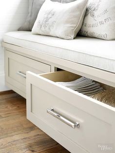 a white bench with drawers underneath it and some pillows on the seat area next to it