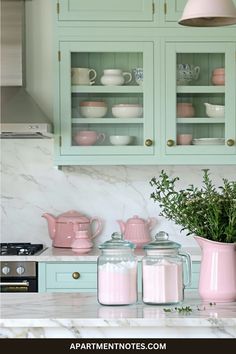 a kitchen with green cabinets and pink pitchers on the counter top, next to a potted plant