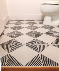 a white toilet sitting in a bathroom next to a tiled floor with black and white designs on it