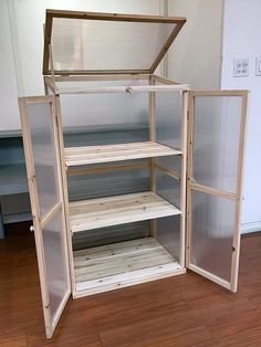 an open refrigerator with shelves inside of it on a hard wood flooring area in front of a white wall