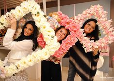 three women holding up flowers in the shape of a heart and smiling at the camera