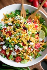 a salad in a white bowl topped with corn, tomatoes, black olives and lettuce