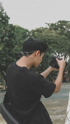 a man holding a camera up to his face while standing in front of a tree