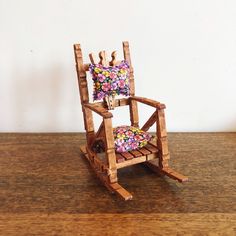 a miniature wooden rocking chair with colorful pillows on it's back and seat cushion