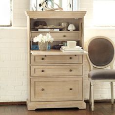 an old dresser with flowers and books on it in front of a chair next to a window