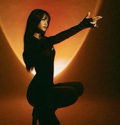 a woman is sitting on the floor with her arms outstretched in front of an orange background