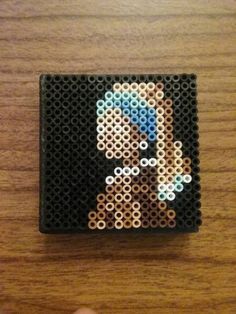 a person is holding a small pixel art piece on a wooden table with their hand