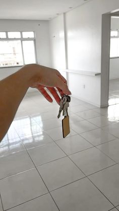 a hand holding a house key in front of a room with white tile flooring