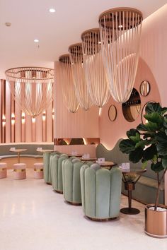 the interior of a modern restaurant with pink walls and green velvet chairs, gold chandeliers hanging from the ceiling