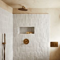 a white tiled shower with gold fixtures and wooden shelves on the wall next to it