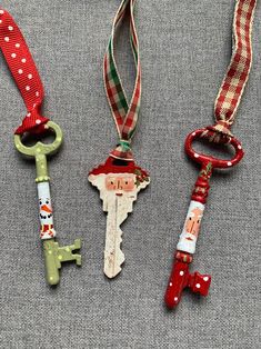 three christmas themed keychains are hanging on a gray surface with red and green ribbons