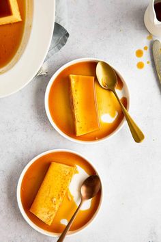 two bowls filled with soup and spoons on top of a white table next to each other